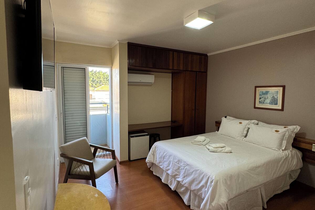 A bedroom with a bed, a desk, a chair, and a small table.