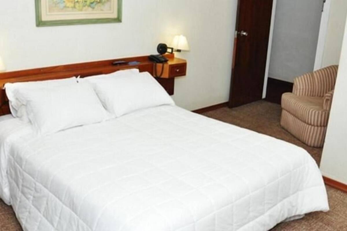 A neatly made bed with white bedding in a hotel room.