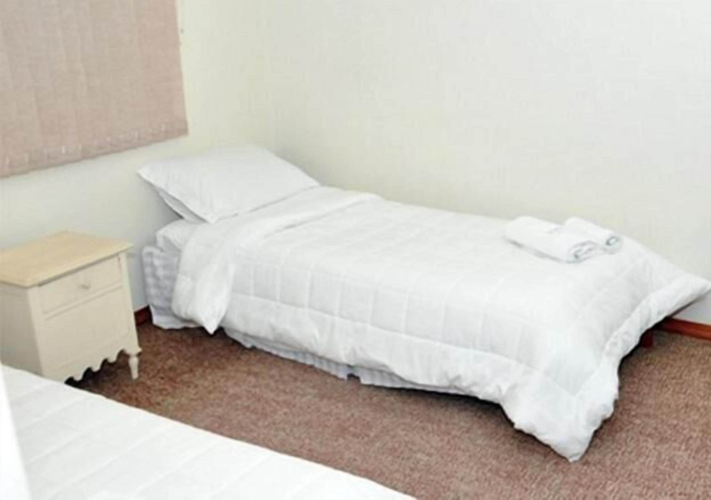 A small, neatly made bed with white bedding in a simple room.