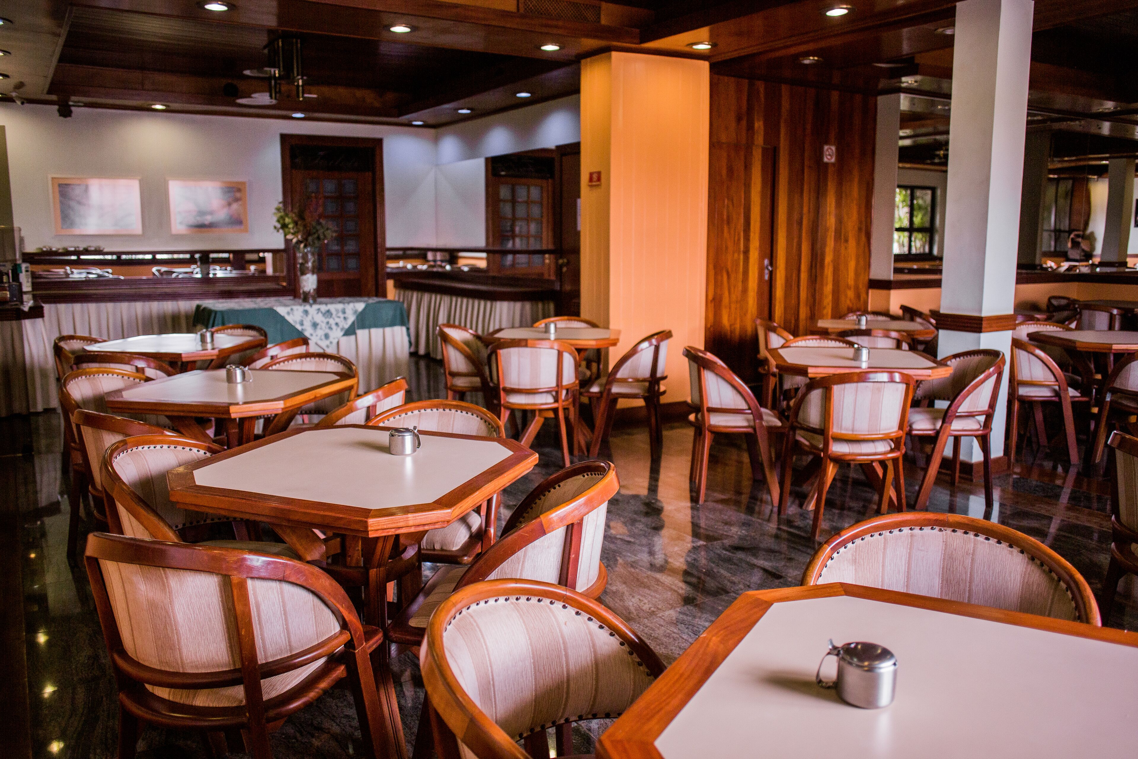 Un restaurant avec des tables et des chaises en bois, un coin bar et une vue sur la cuisine.