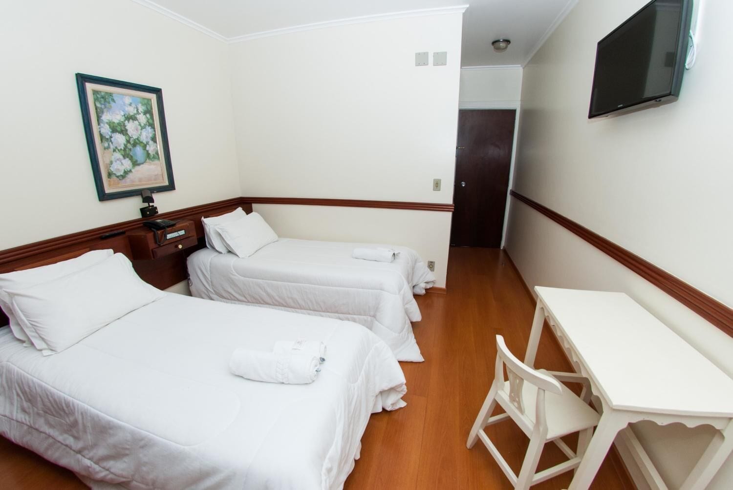 A hotel room with two beds, a desk, and a painting on the wall.