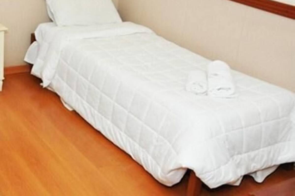 A single bed with white bedding in a room with wooden flooring and a plain wall.