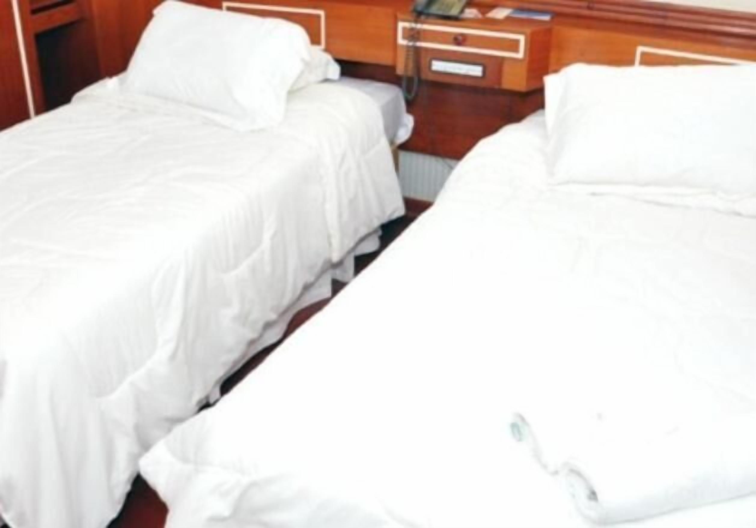Two single beds with white linens in a hotel room.