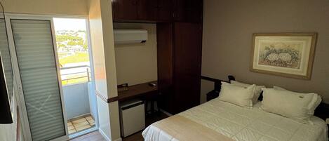 A bedroom with a bed, a desk, a chair, a wardrobe, and a small refrigerator.