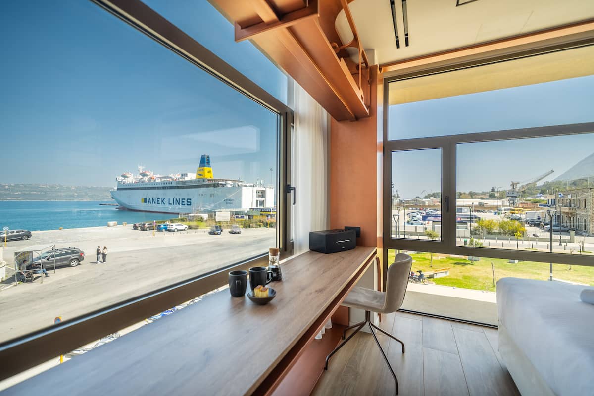A modern hotel room with a large window overlooking a port and a ship named "ANEK LINES".