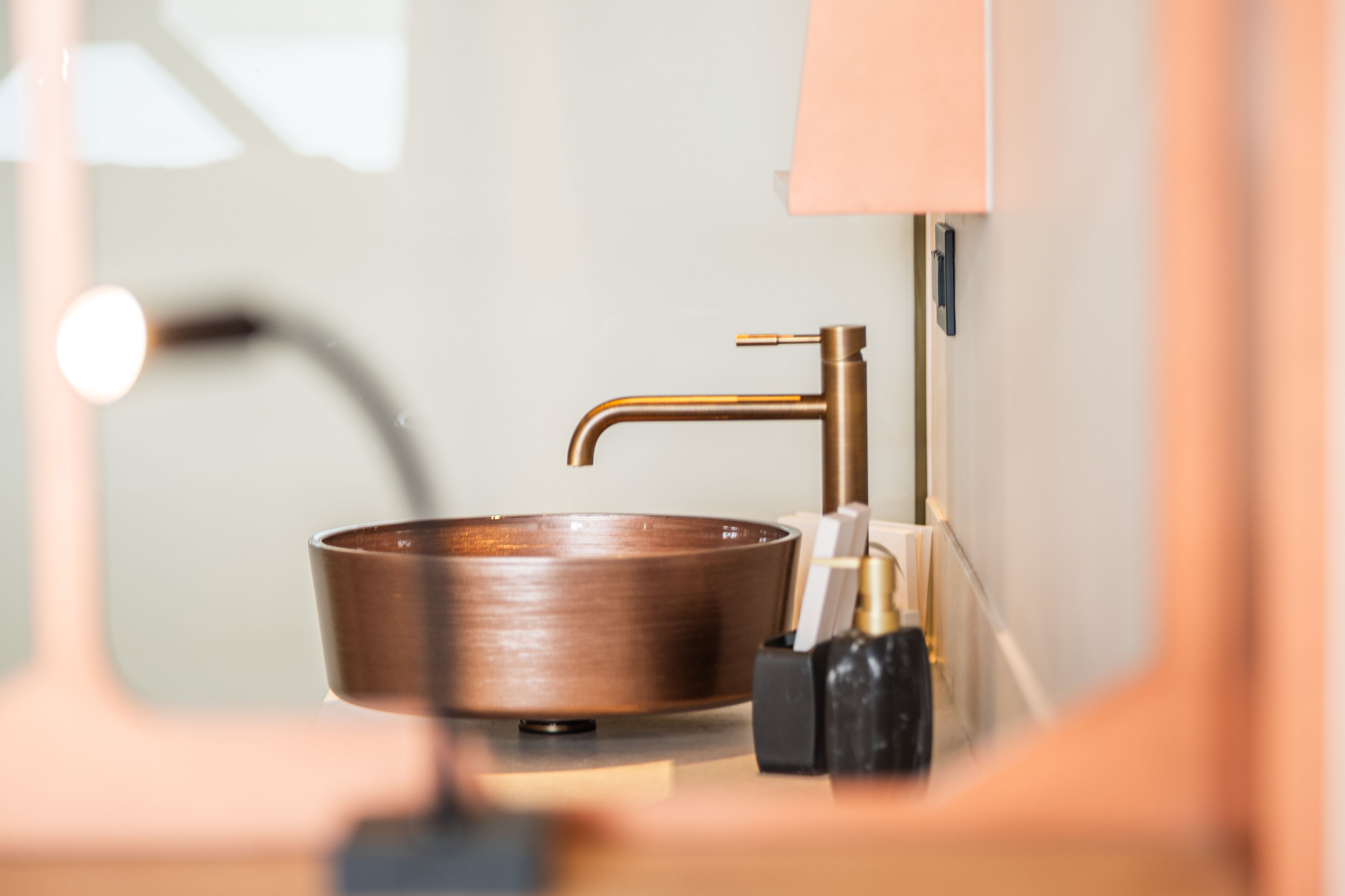A bathroom with a copper sink, a mirror, and a black soap dispenser.