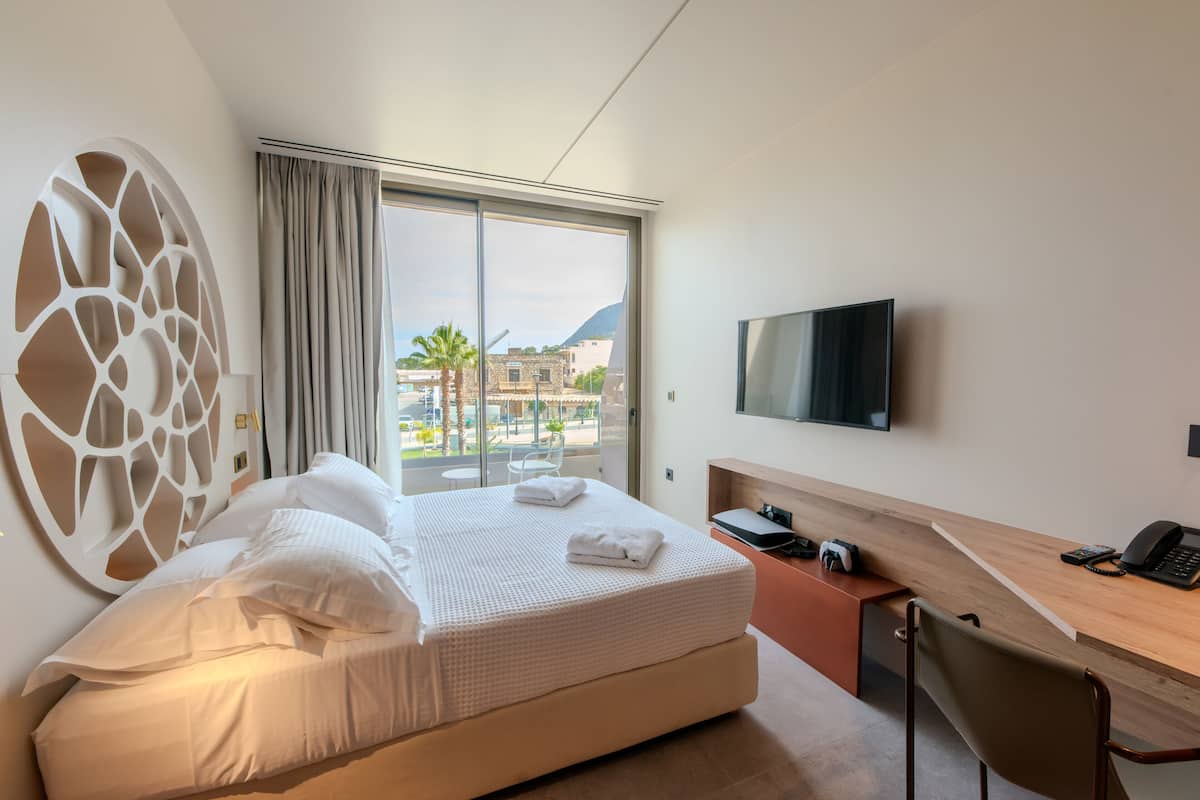 A modern hotel room with a large bed, a desk, a TV, and a view of the city.