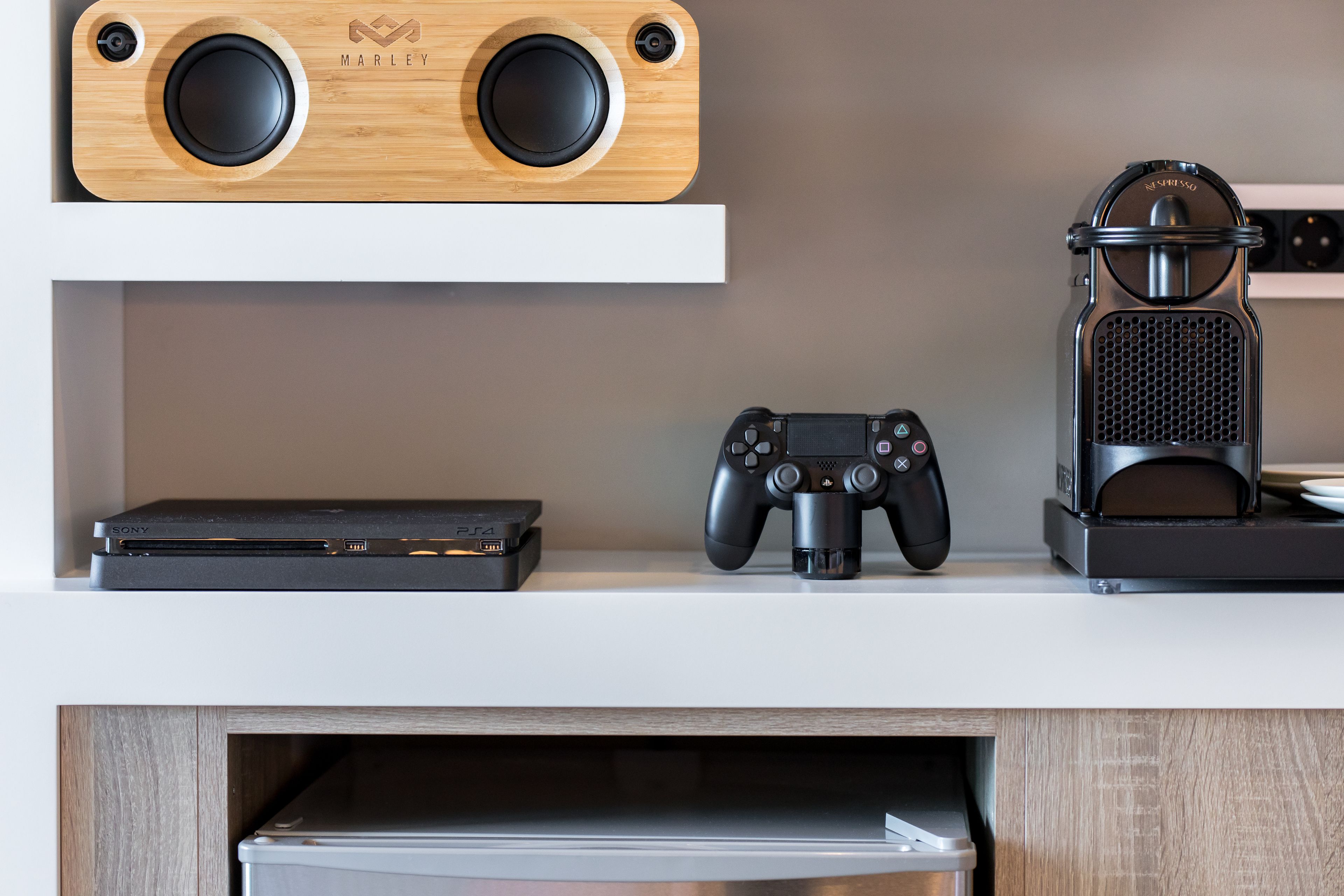 En hylla med en högtalare i trä, en PlayStation 4-konsol och en spelkontroll.