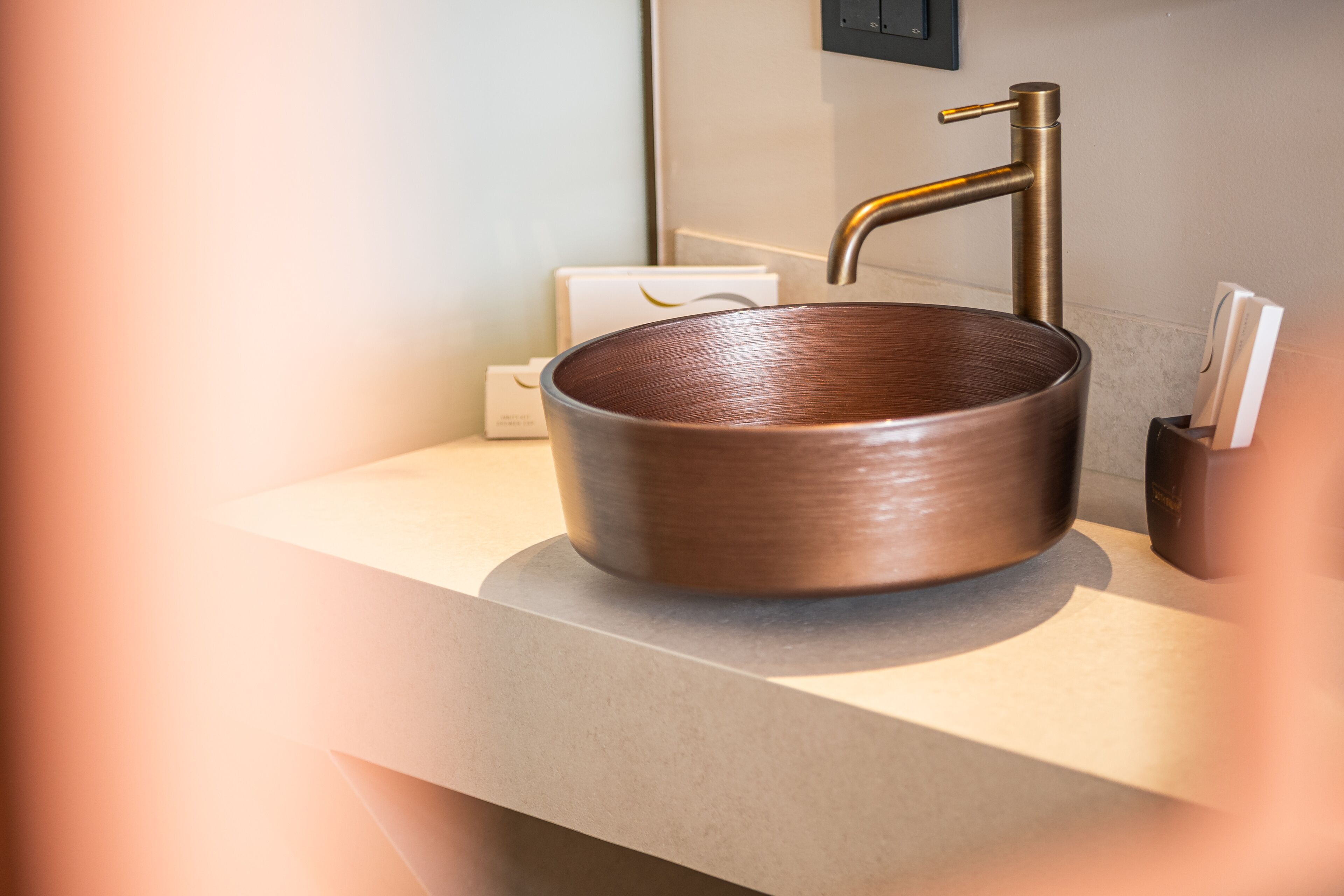 A modern bathroom with a copper sink, a towel dispenser, and a mirror.