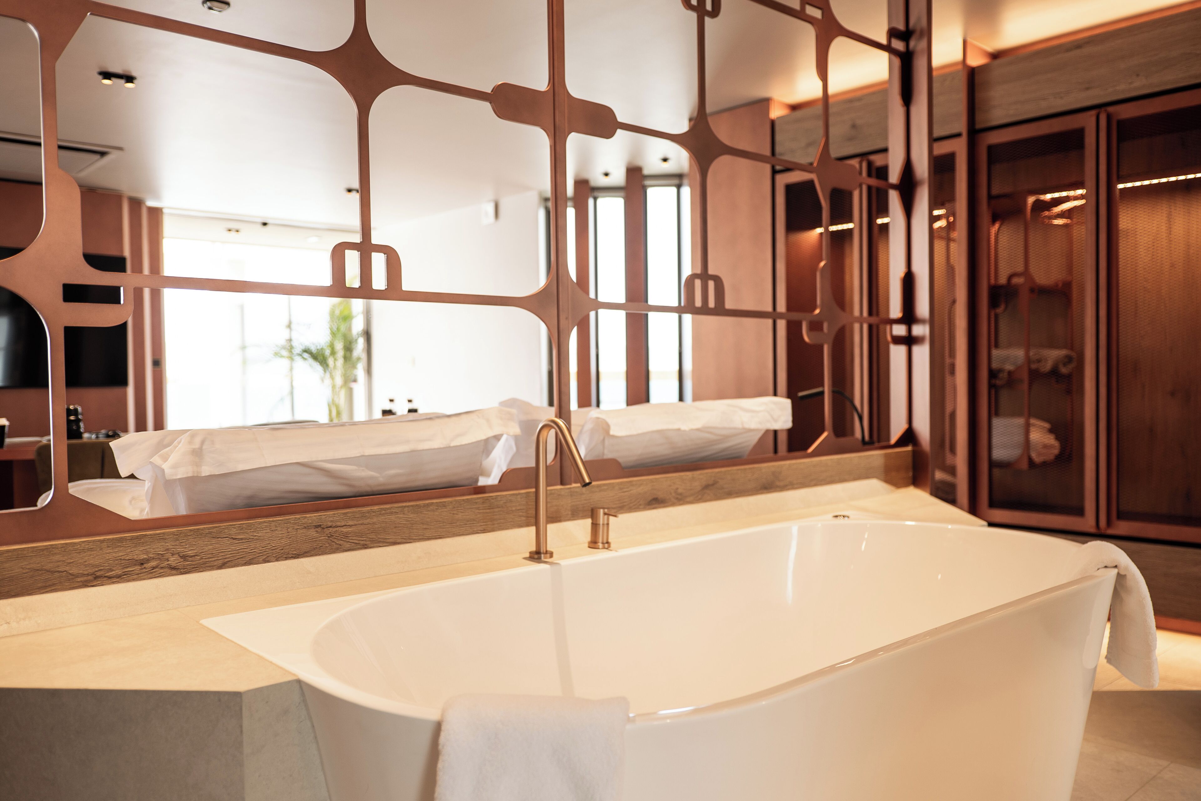 A modern bathroom with a freestanding bathtub, a large mirror, and wooden cabinetry.