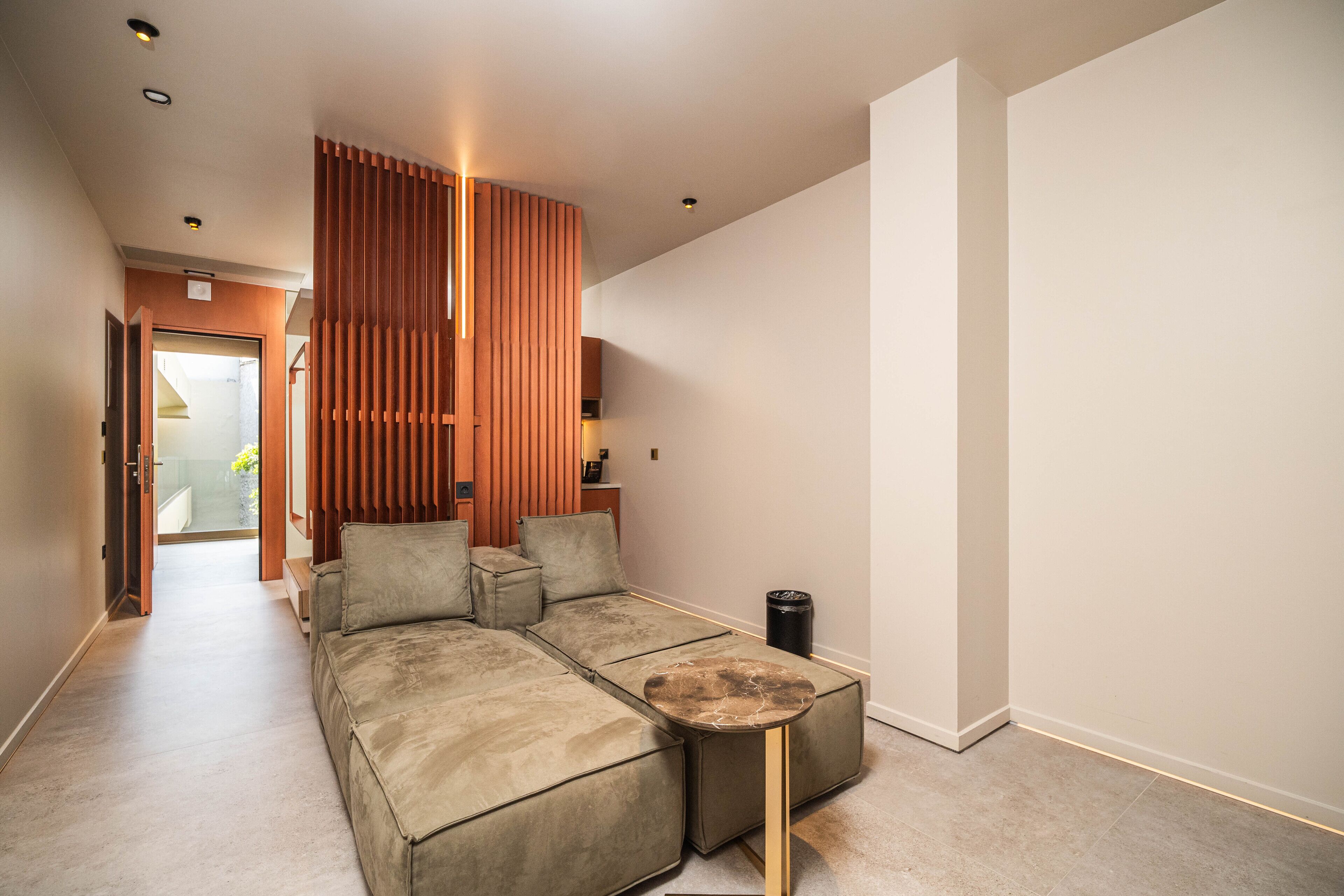 Un salon moderne avec un canapé d’angle, une table basse ronde et un claustra en bois.