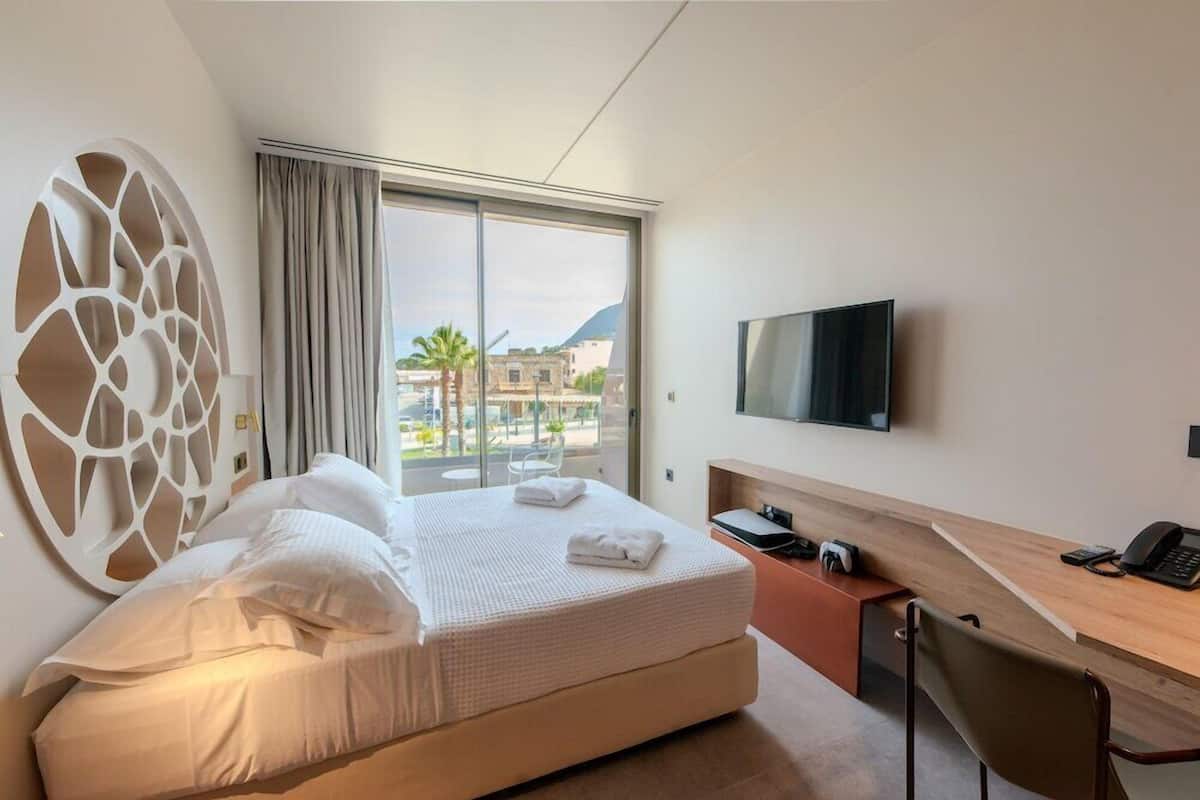 A hotel room with a bed, a desk, a TV, and a large window with a view.
