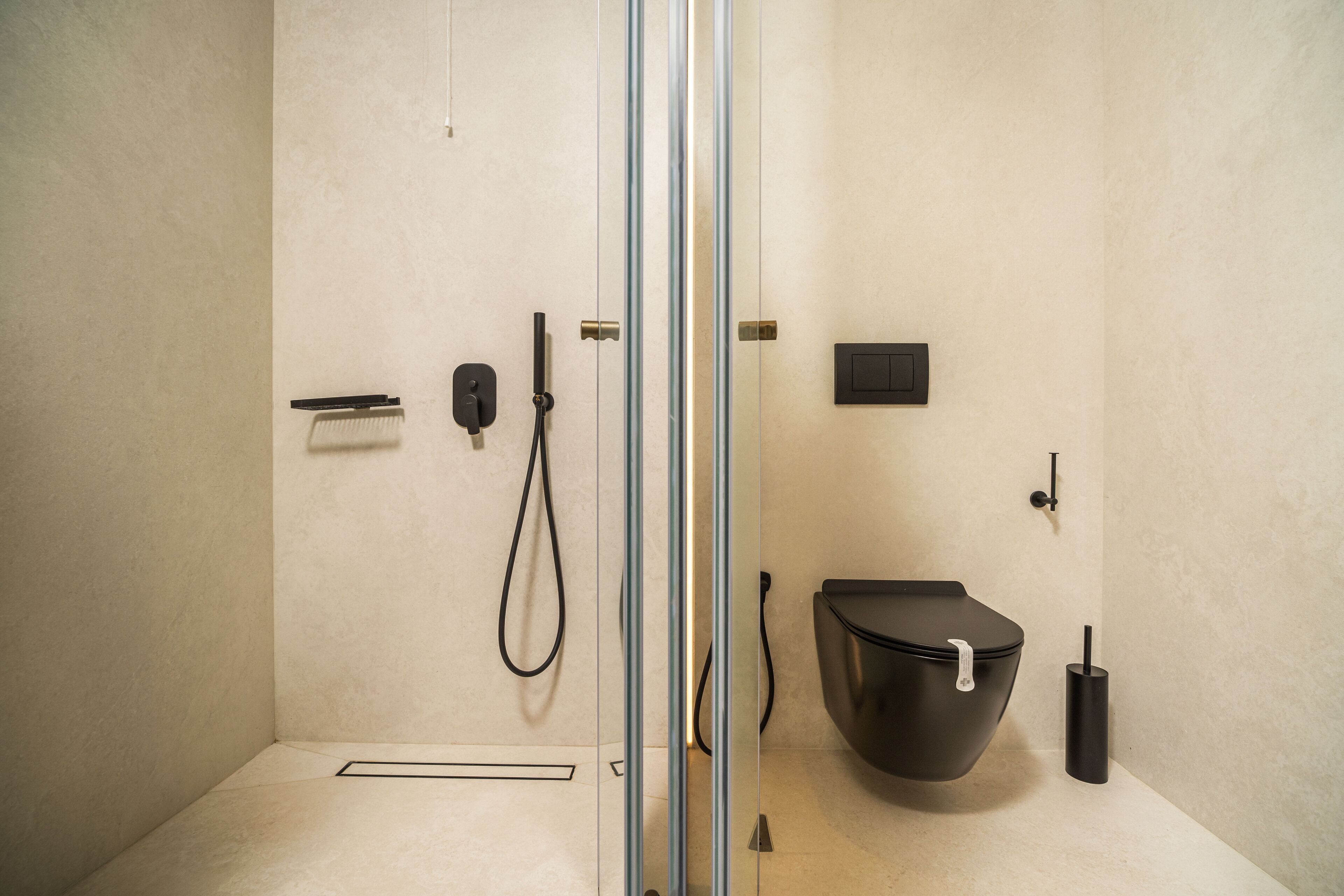 A modern bathroom with a glass shower enclosure, a black toilet, and a handheld showerhead.