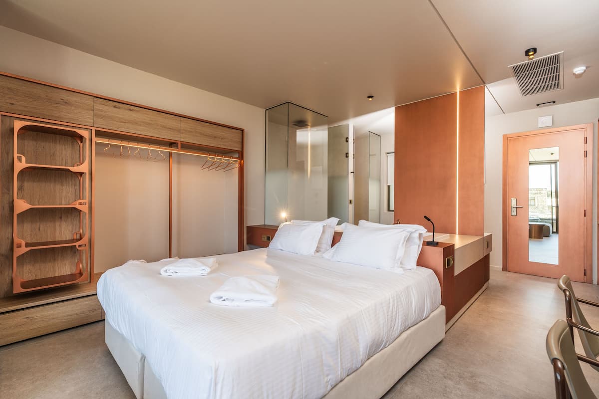 A modern hotel room with a large bed, a wooden wardrobe, a mirror, and a desk.