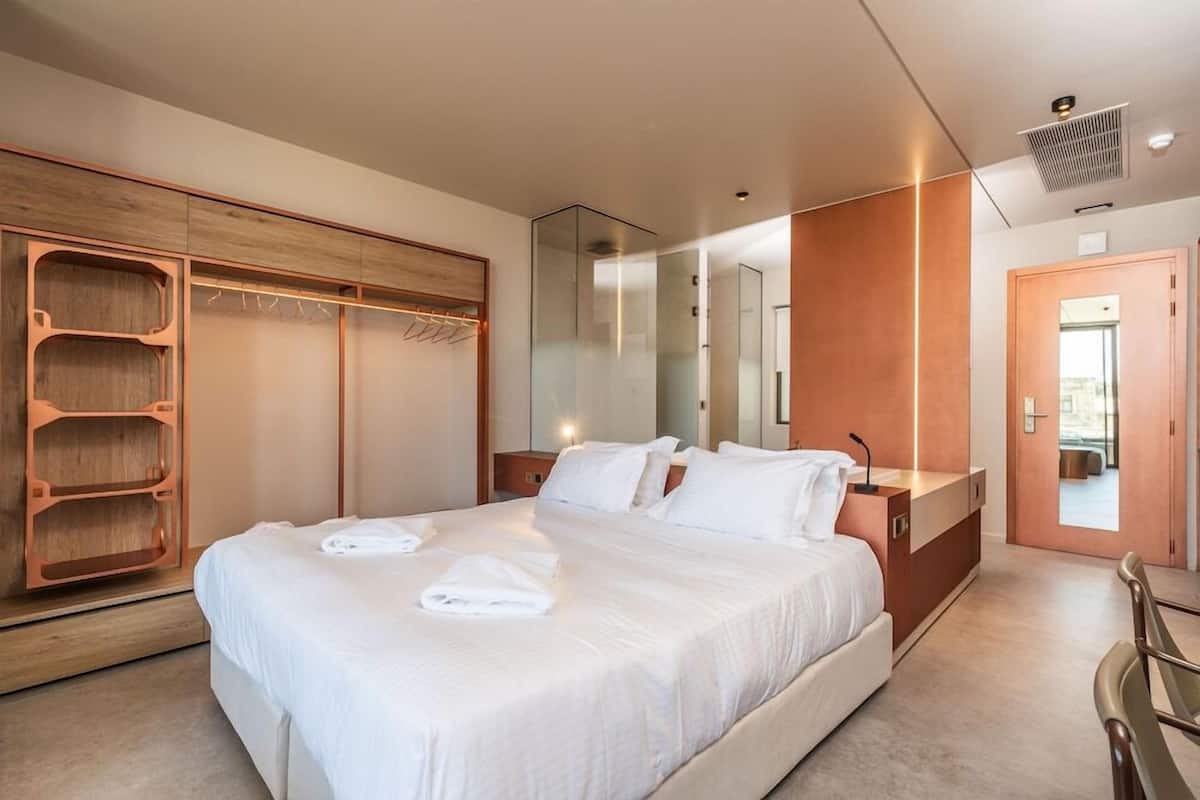 A modern hotel room with a large bed, a wooden wardrobe, a mirror, and a desk.