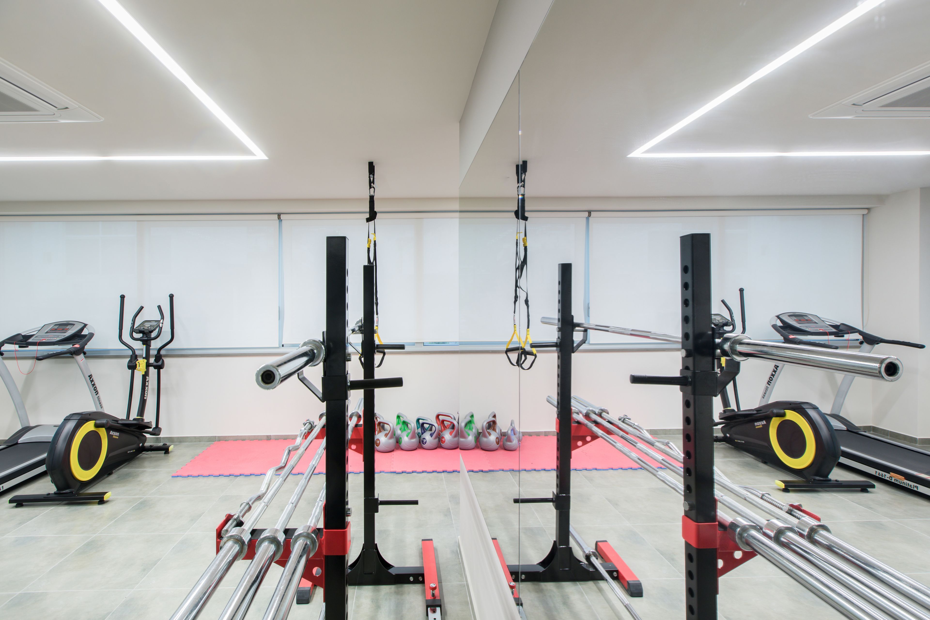 Un gimnasio con cintas de correr, una zona de levantamiento de pesas y un área con colchonetas rojas.
