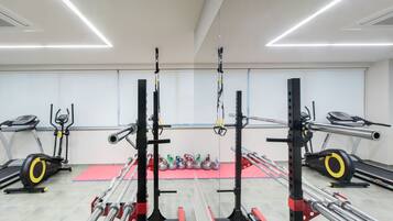 Un gimnasio con cintas de correr, una zona de levantamiento de pesas y un área con colchonetas rojas.