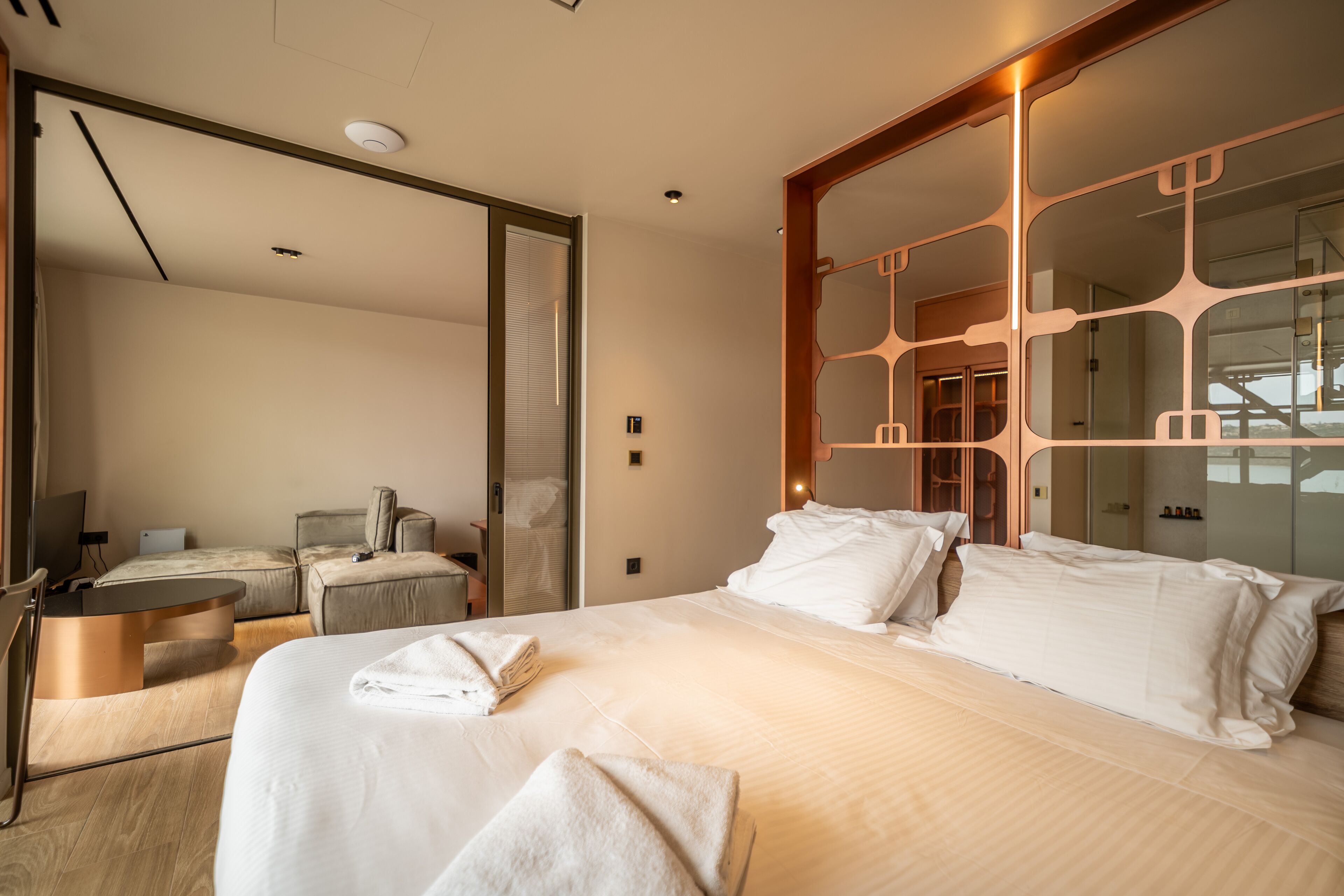 Quarto de hotel moderno com uma cama grande, uma escrivaninha, uma cadeira e um espelho.