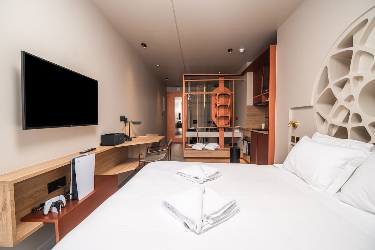 A modern hotel room with a large bed, a flat-screen TV, a wooden desk, and a seating area.