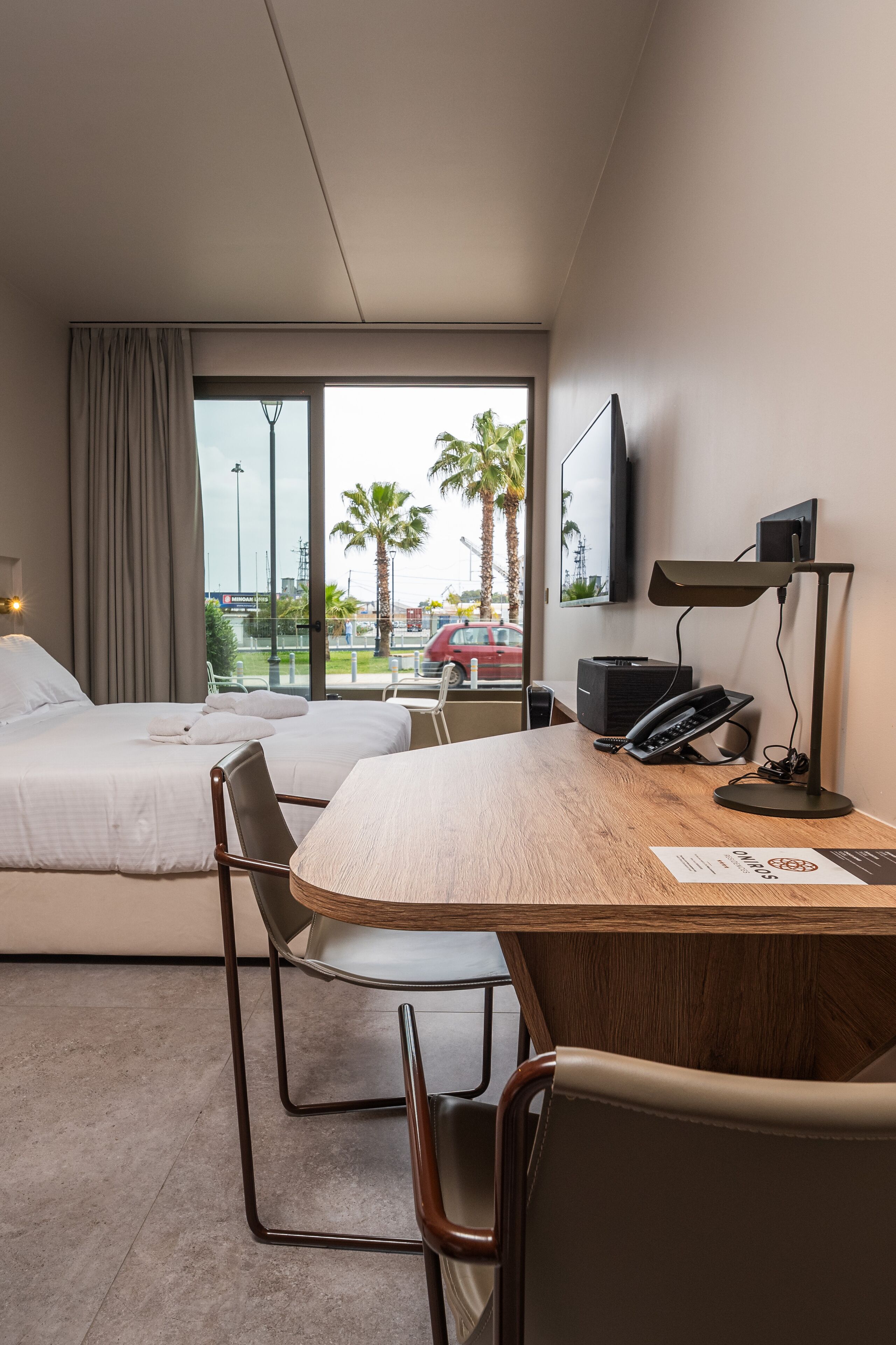 Una habitación de hotel con dos camas, un escritorio con computadora, una lámpara y un televisor.