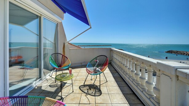 Een balkon met uitzicht op zee, voorzien van een witte balustrade en een blauw zonnescherm.