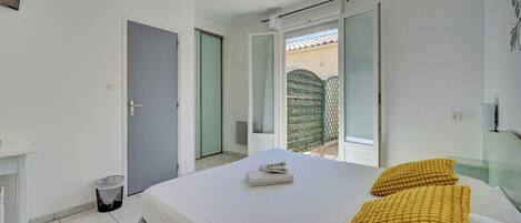 Een slaapkamer met een bed, twee kussens, een tafeltje, een prullenbak en een schuifdeur naar een balkon.