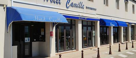 A building with a sign reading "Hotel Camille" and blue awnings.