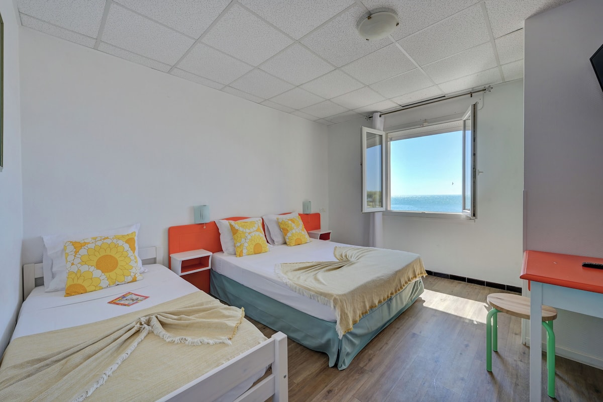 A hotel room with two beds, a desk, and a window with a view.
