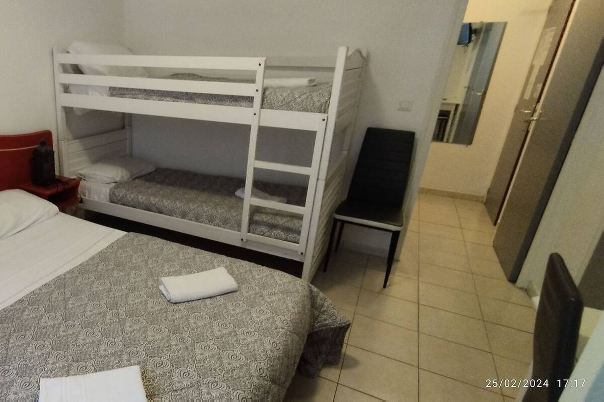 A hotel room with a red headboard bed, a bunk bed, a small table, and a mirror.