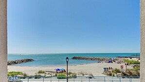 Uitzicht op een strand met een rotsenrij en een helderblauwe lucht, waar enkele mensen ontspannen.