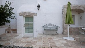 Une cour avec un mur blanc, une porte verte, un banc en métal et un parasol vert.