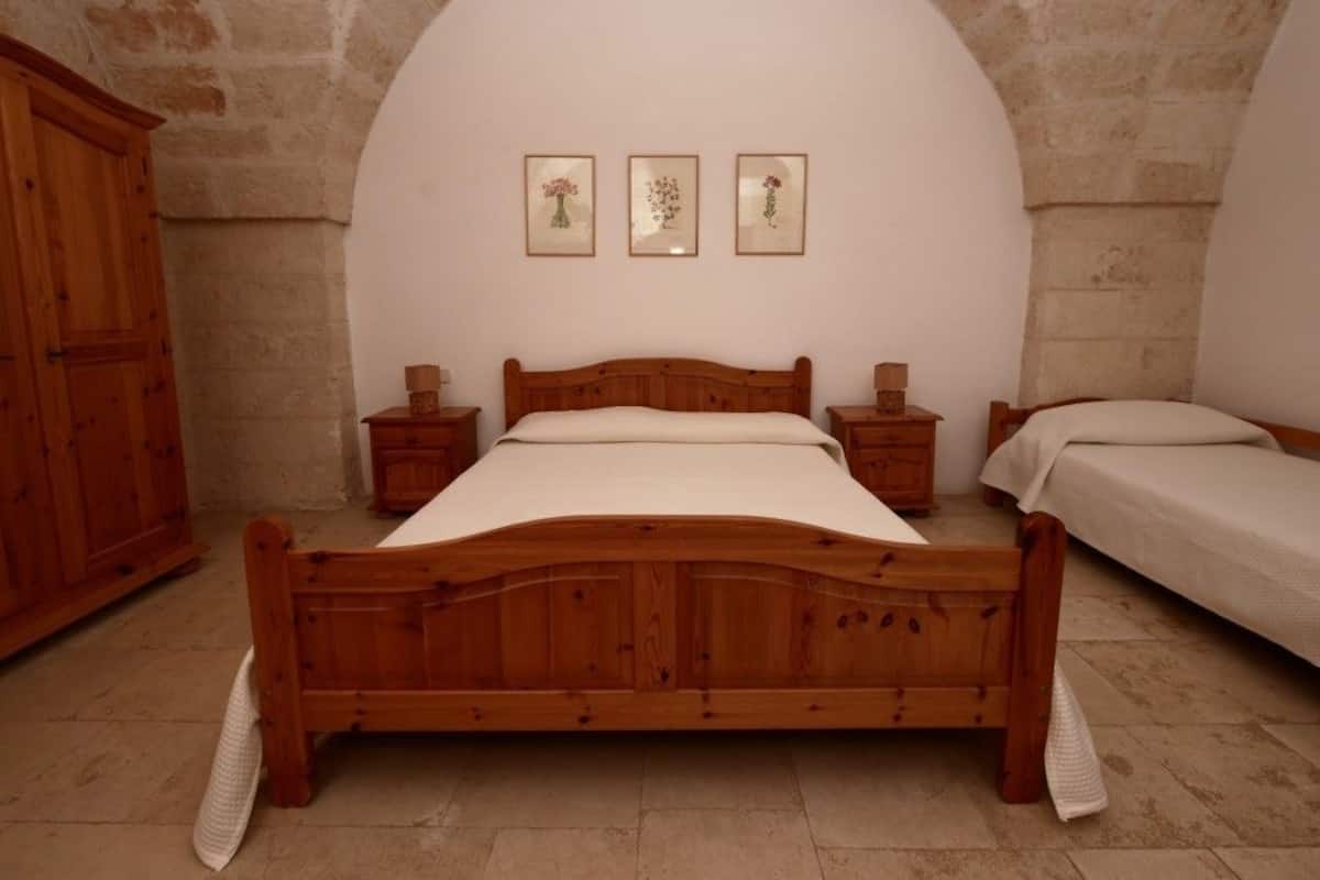 A bedroom with a wooden bed, a nightstand, a dresser, and a small table. There are three framed pictures on the wall.