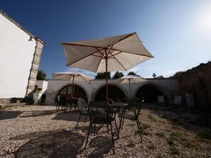 An outdoor seating area with tables and chairs, umbrellas, and a building with arched doorways. - Masseria Maccarone (Fasano)