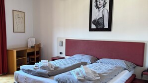Cama doble con cabecera roja, mesita de noche con lámpara y un cuadro colgado en la pared.
