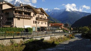 Un hotel con balcón, un río al frente y montañas al fondo.