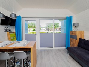 A room with a dining table, chairs, a sofa, a TV, and a view of the outside. - Balticus (Postomino)