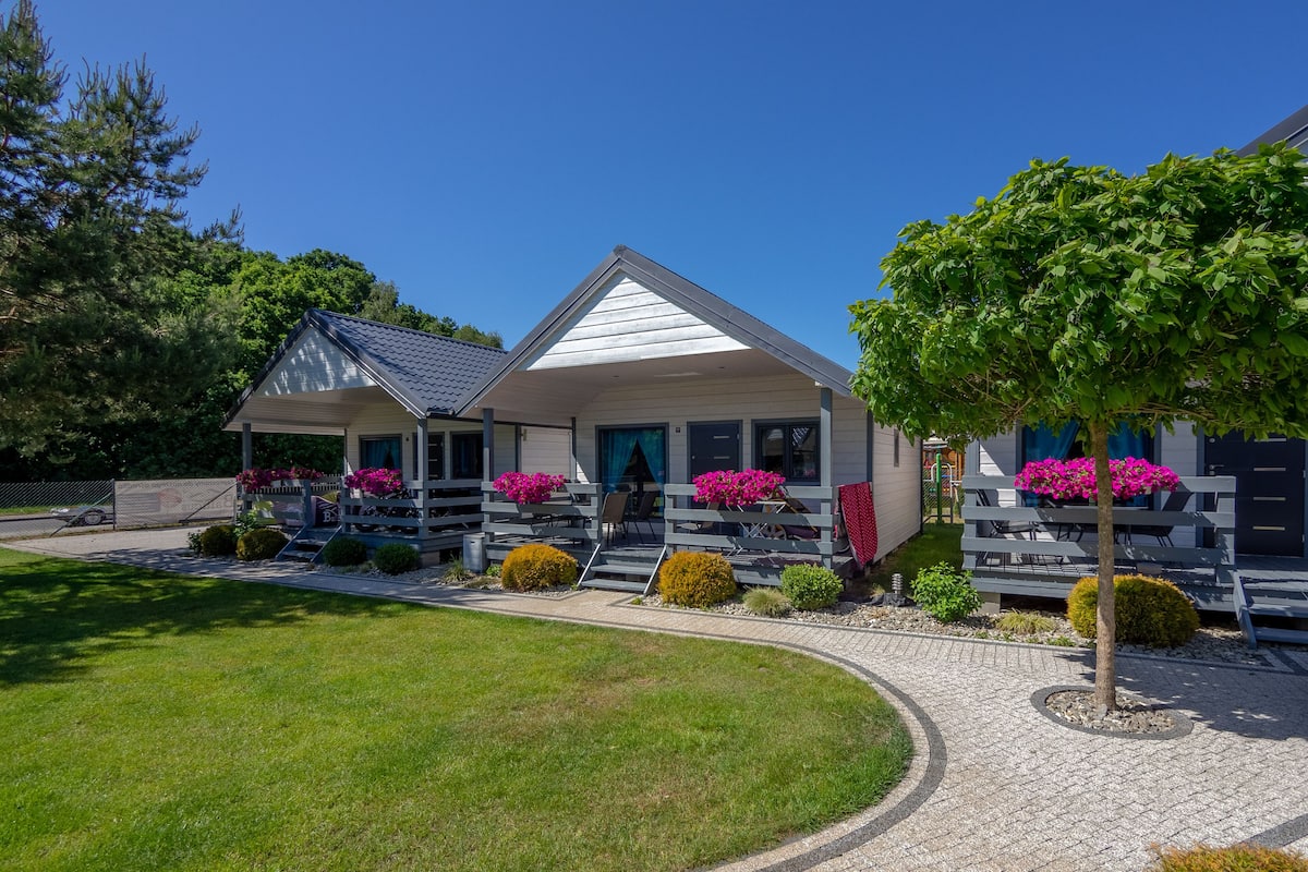 A two-story lodge with a covered porch, outdoor seating, and flower arrangements.