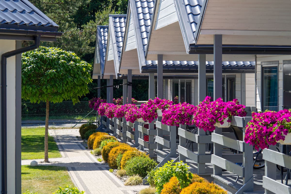 A row of modern buildings with a covered walkway, surrounded by well-maintained landscaping and vibrant flower beds.