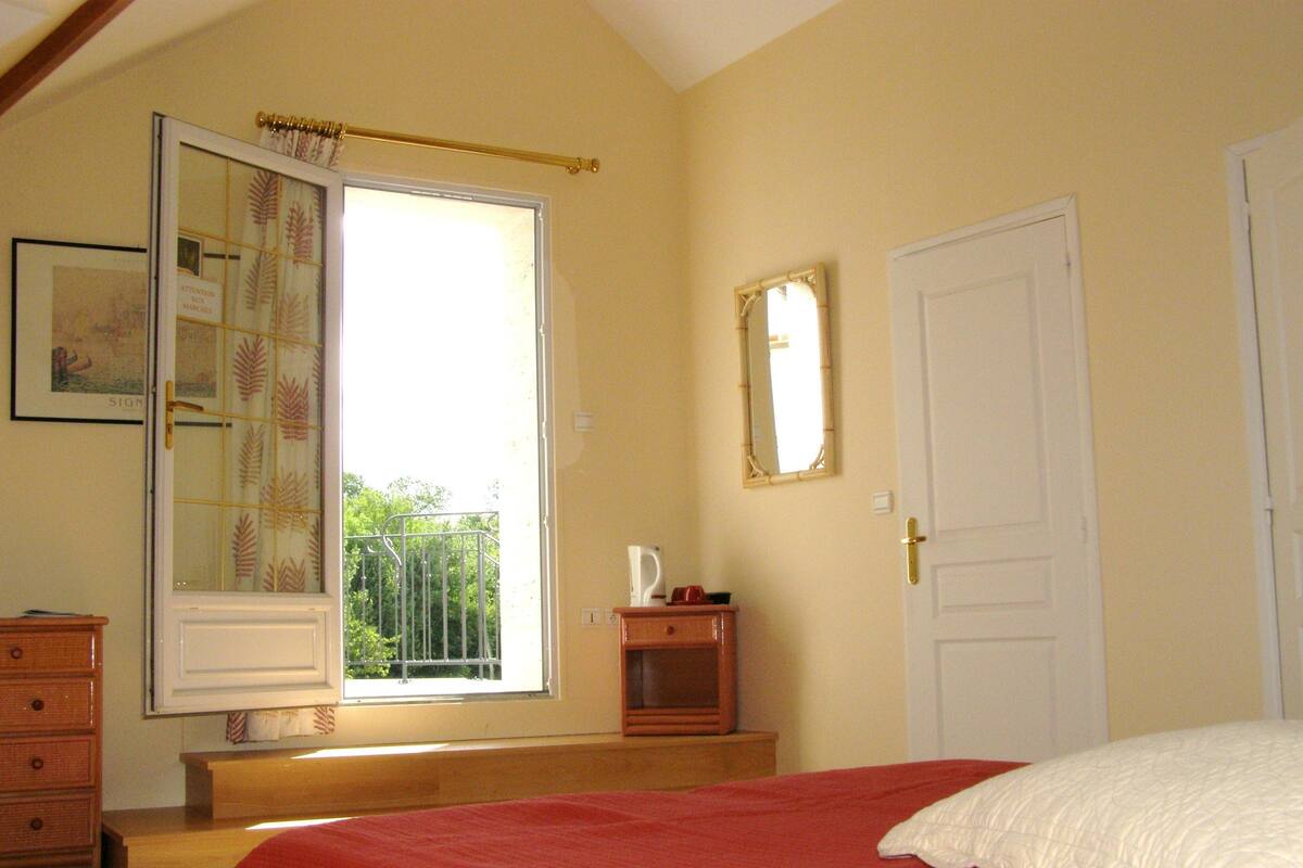 A bedroom with a bed, a dresser, a window with a view, a door, and a mirror.