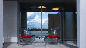 A modern outdoor seating area with two transparent chairs and a small table, overlooking a body of water and a cloudy sky. - La Perla (Camerano)