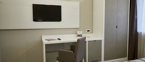 A hotel room with a bed, a desk, a chair, a television, and a wardrobe.