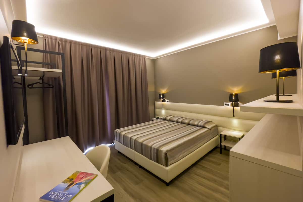 A modern hotel room with a large bed, bedside tables, a desk, and a chair.