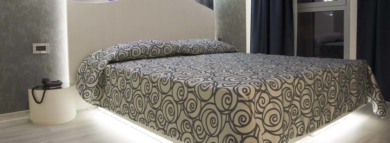A modern bedroom with a patterned bedspread, a bedside table with a lamp, and a view of a balcony.
