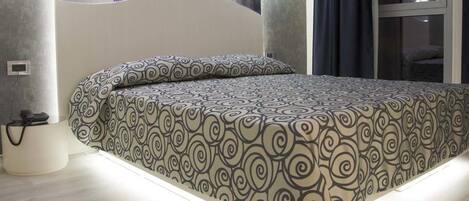 Un dormitorio moderno con una colcha estampada, una mesita de noche con lámpara y vistas a un balcón.