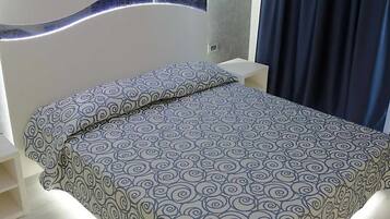 Une chambre moderne avec une couvre-lit à motifs, une table de chevet avec un téléphone et une tête de lit dotée d’un luminaire.