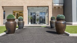 A hotel entrance with a brick facade, large potted plants, and a glass door. - La Perla (Camerano)