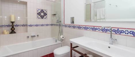 A bathroom with a bathtub, toilet, and sink, featuring white tiles with blue and red decorative borders.
