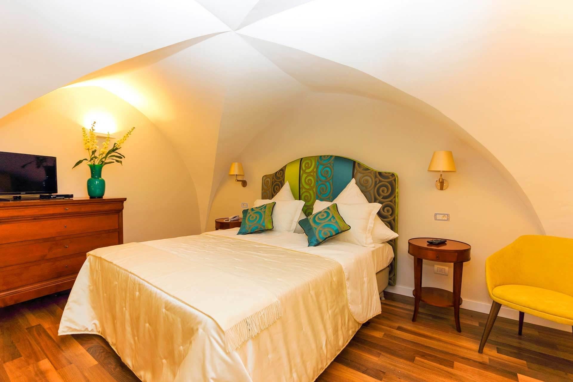 Quarto com cama, televisão, cómoda de madeira, cadeira amarela e candeeiro.