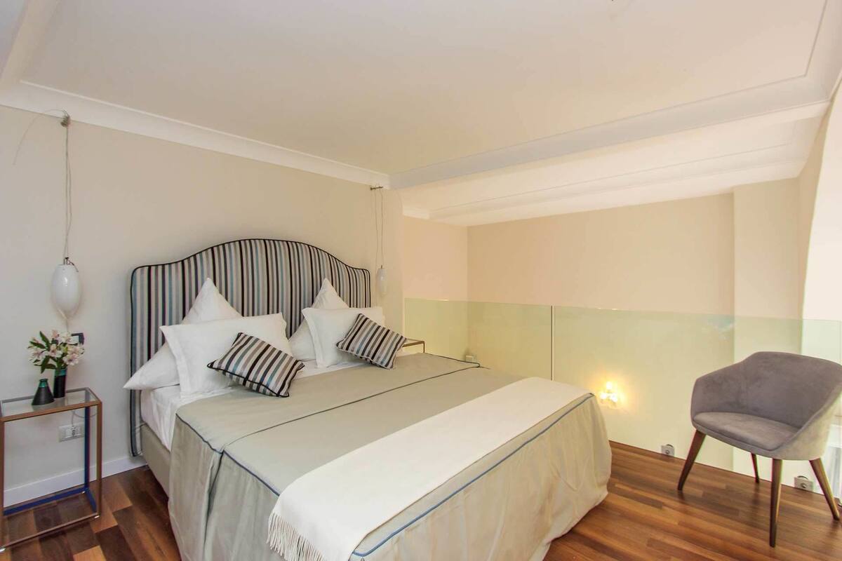 A bedroom with a bed, bedside table, lamp, chair, and a small table with flowers.