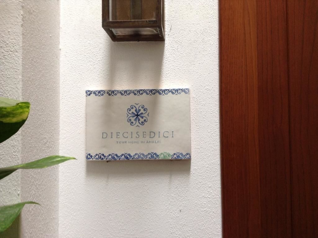 A sign with the text "DIECISEDICI YOUR HOME IN AMALFI" on a white wall.